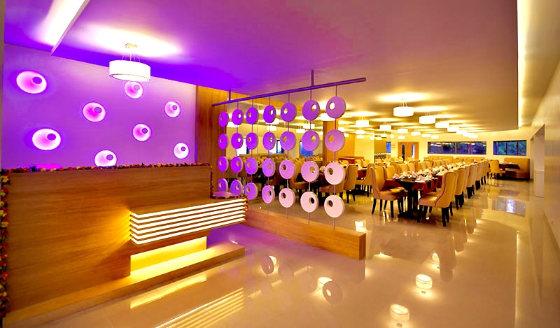  Elegant dining room interior with vibrant lighting at United 21 Resort in Kodaikanal. Features
                contemporary design with purple wall lights, hanging decor, and well-arranged dining tables.