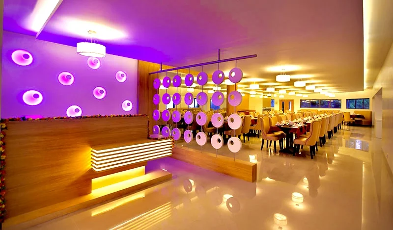  Elegant dining room interior with vibrant lighting at United 21 Resort in Kodaikanal. Features
                contemporary design with purple wall lights, hanging decor, and well-arranged dining tables.